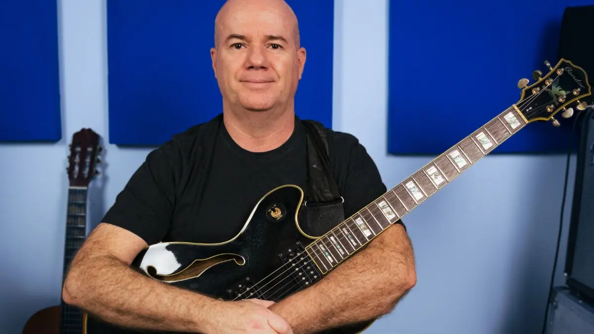 Professor Armando Leite segurando guitarra elétrica em seu estúdio de música.